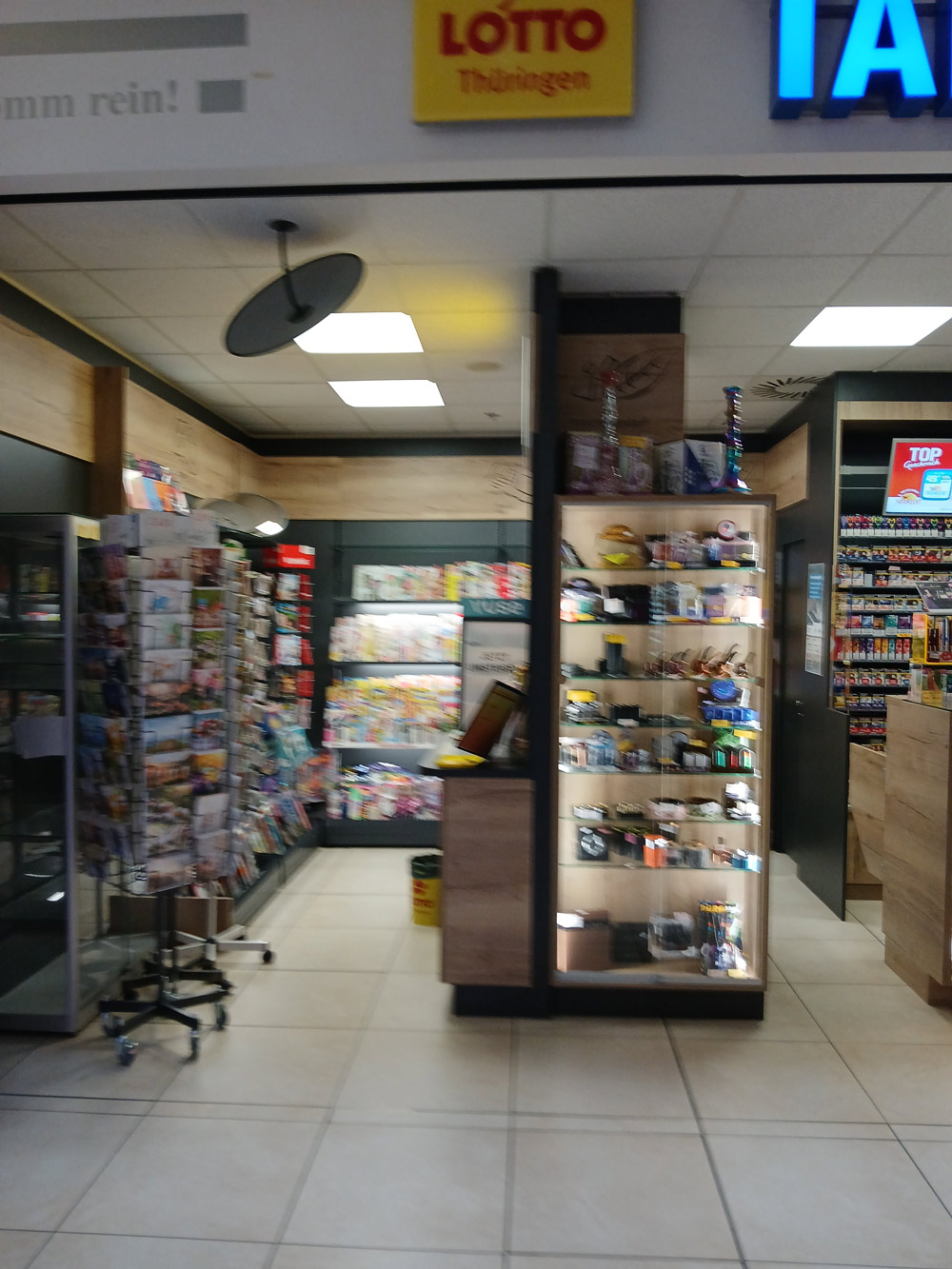 Ein gut beleuchteter Kiosk mit Zeitschriftenregal, Lotto Schild und bunten Waren